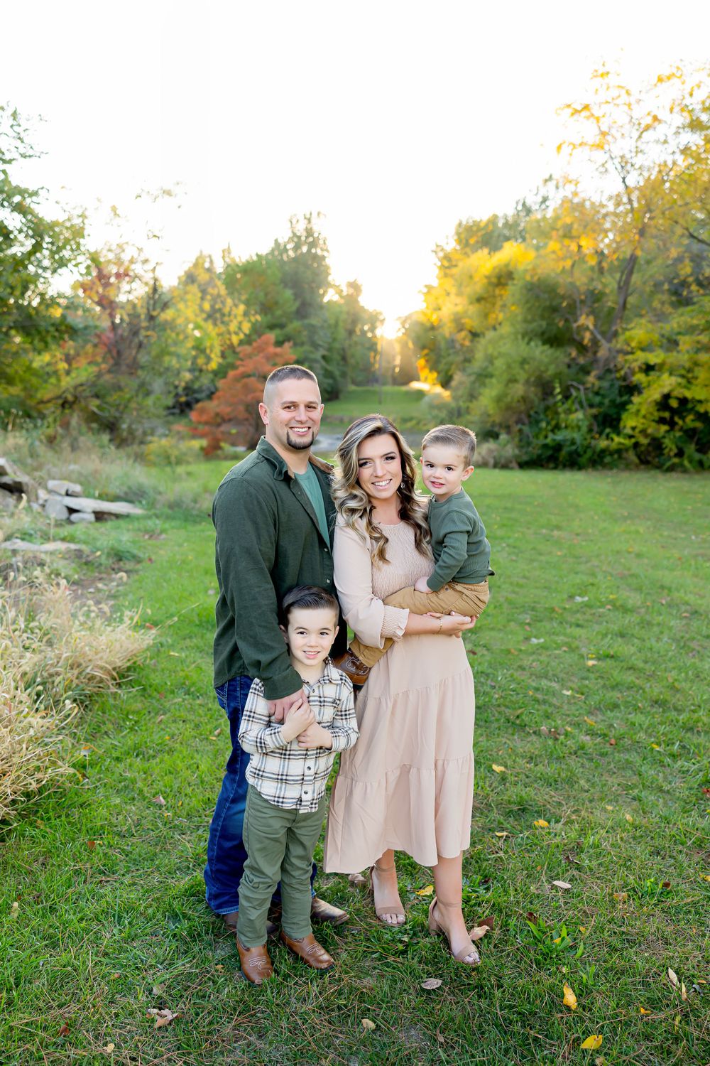 A family of four poses together outdoors during autumn golden hour.