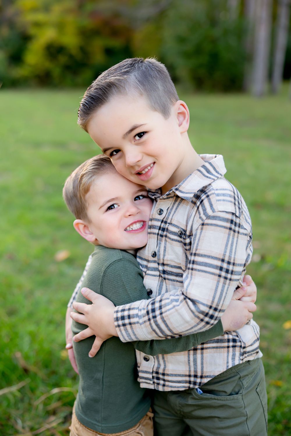 Two young children embracing and smiling outdoors in casual clothing.