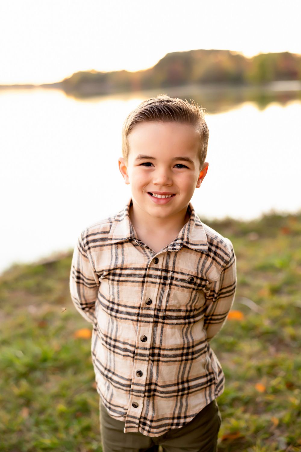 A young person in a plaid shirt smiling outdoors during golden hour.