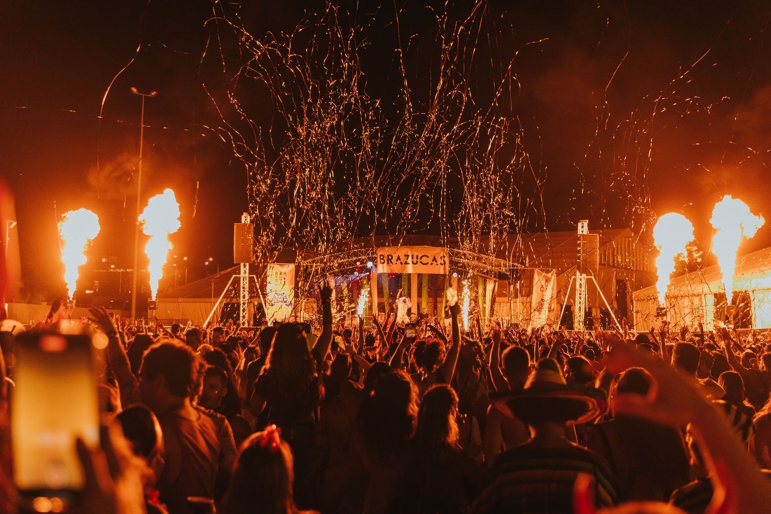 Dramatic concert scene with fire effects and crowd silhouettes against dark sky.