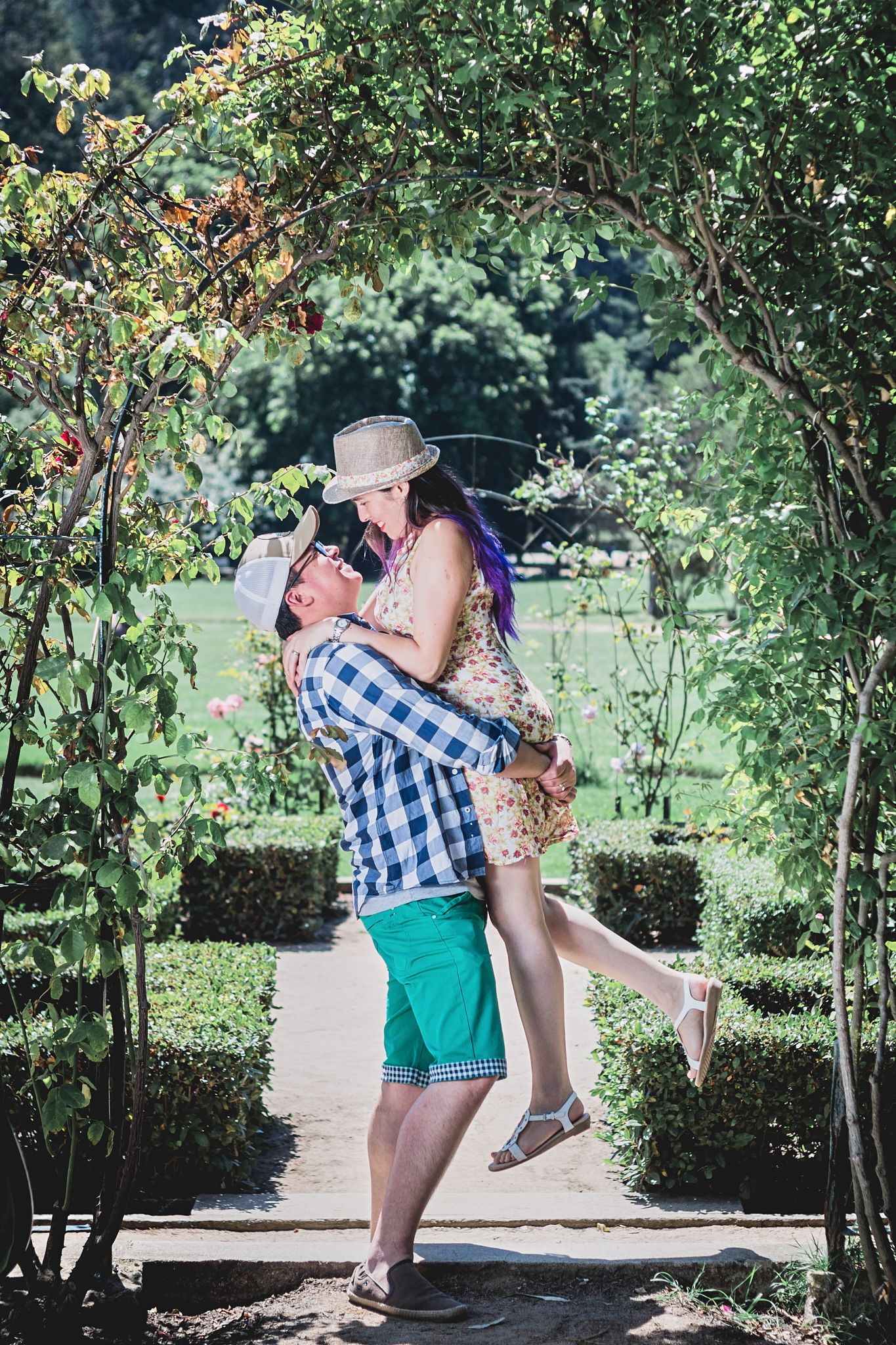 Playful couple embracing under garden archway during summer photoshoot.