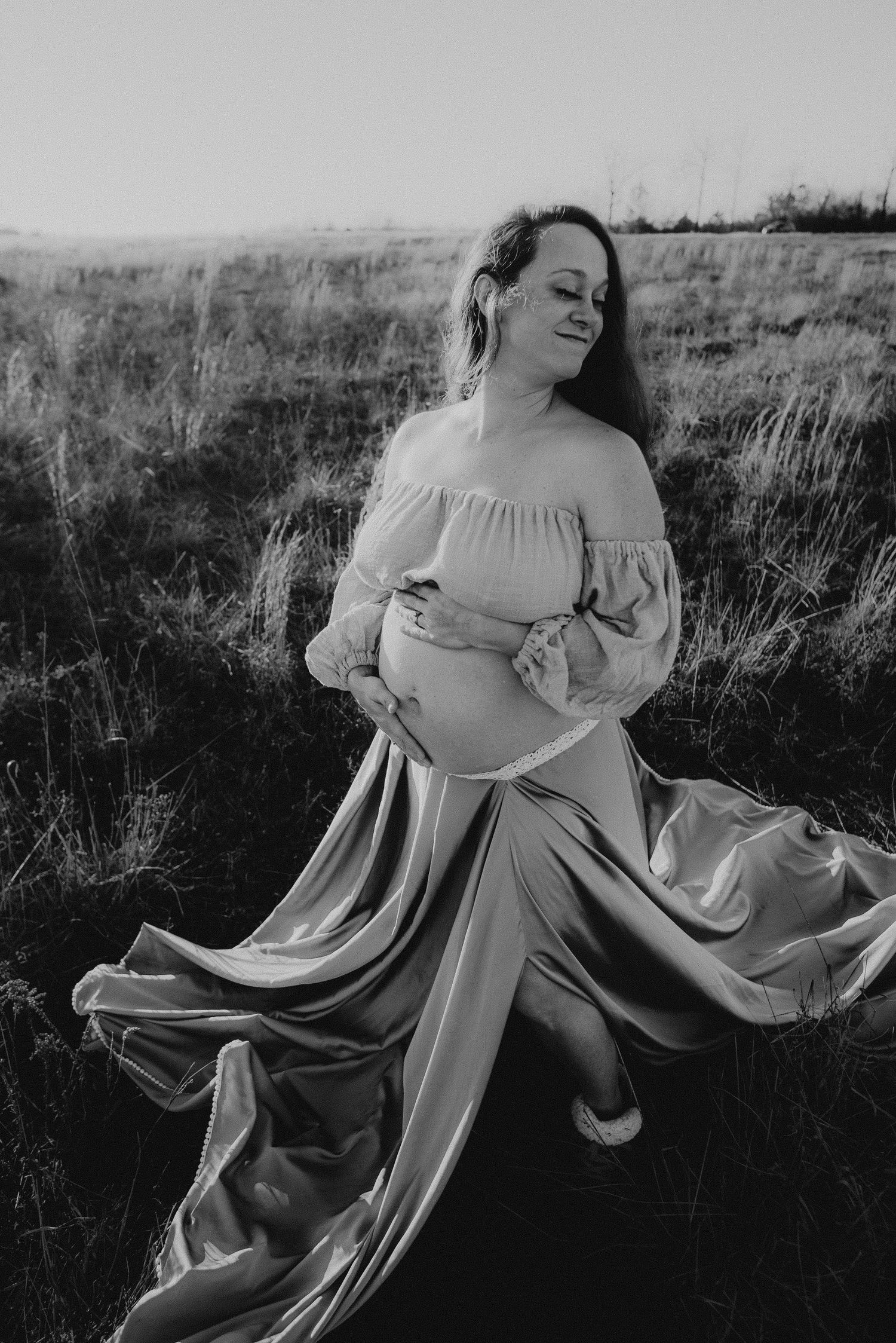 Artistic black and white portrait showing flowing fabric movement in a natural field setting.