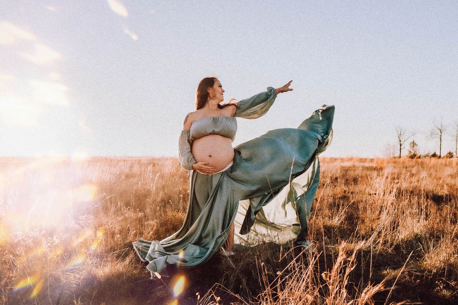 A flowing blue dress billows in the wind against a golden sunset field of tall grass.