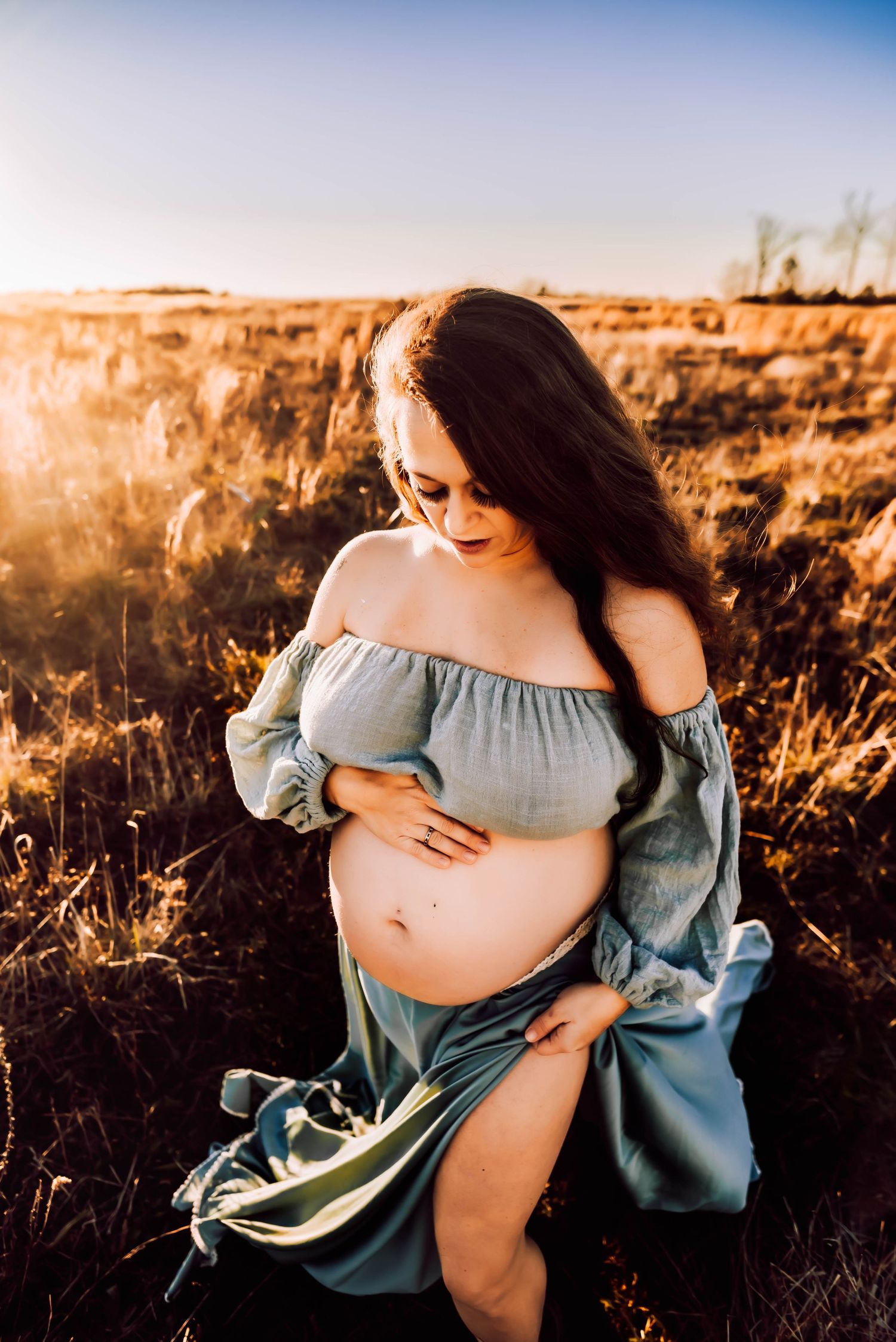 Ethereal maternity photoshoot in a field at golden hour with flowing blue fabric.