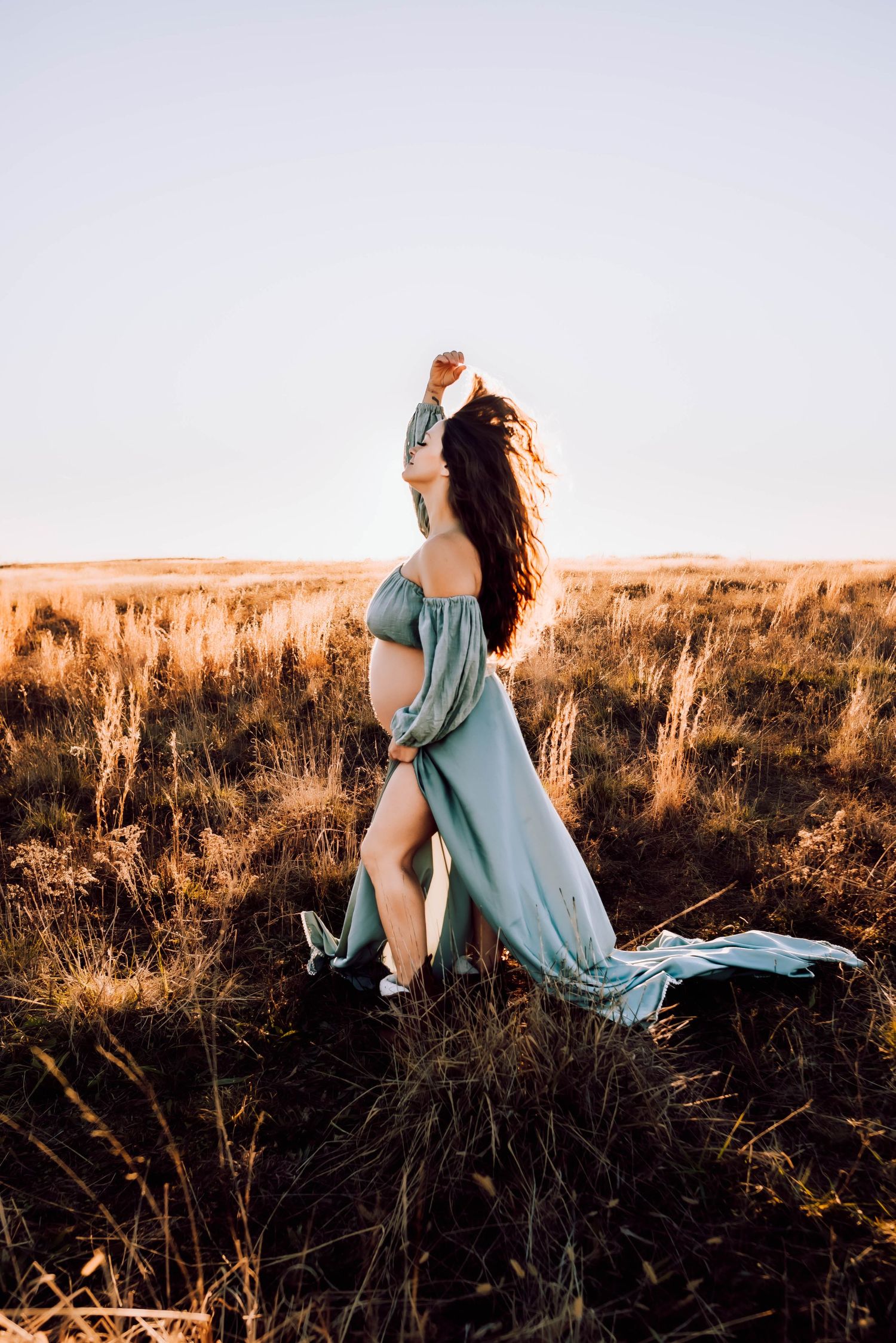 Dramatic pose in a light blue dress against sunset-lit grassland.