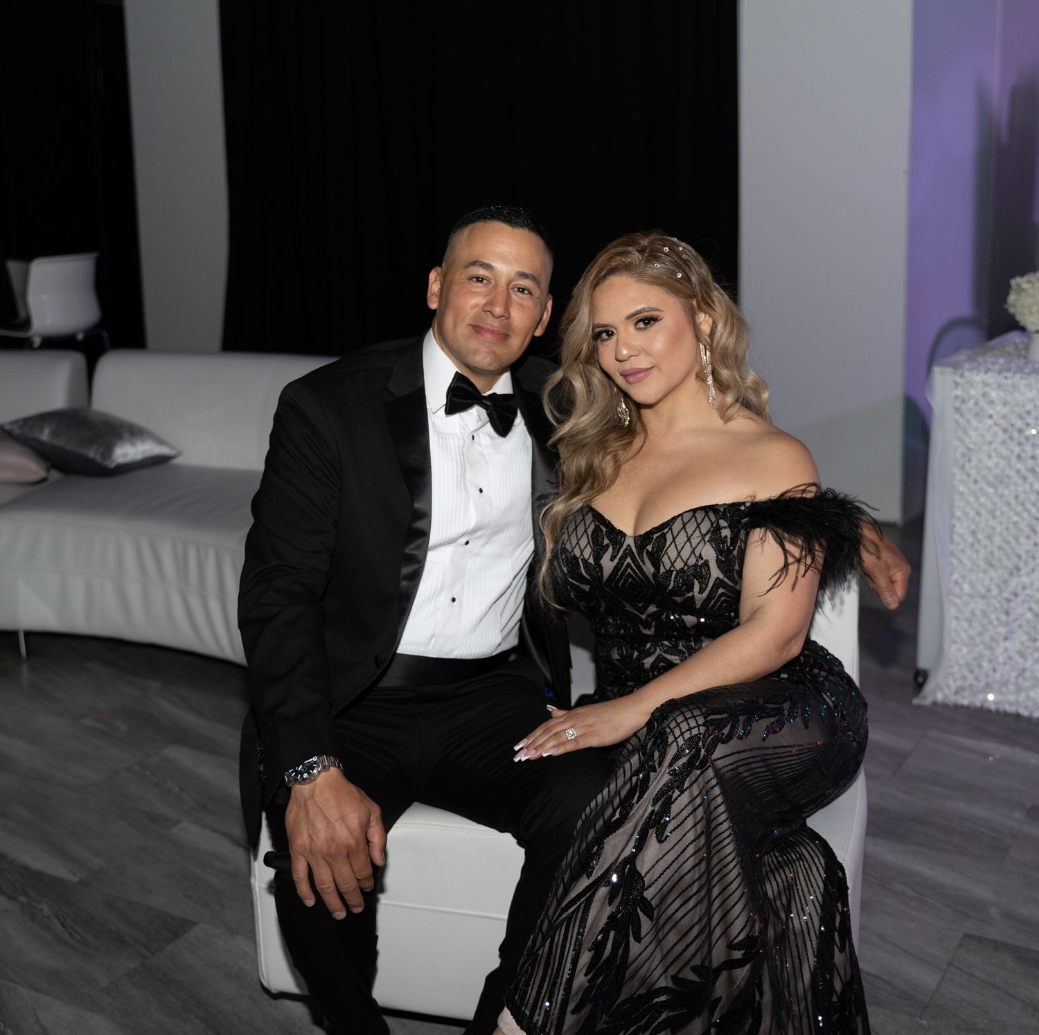 Formal couple posing on white furniture at an elegant event.