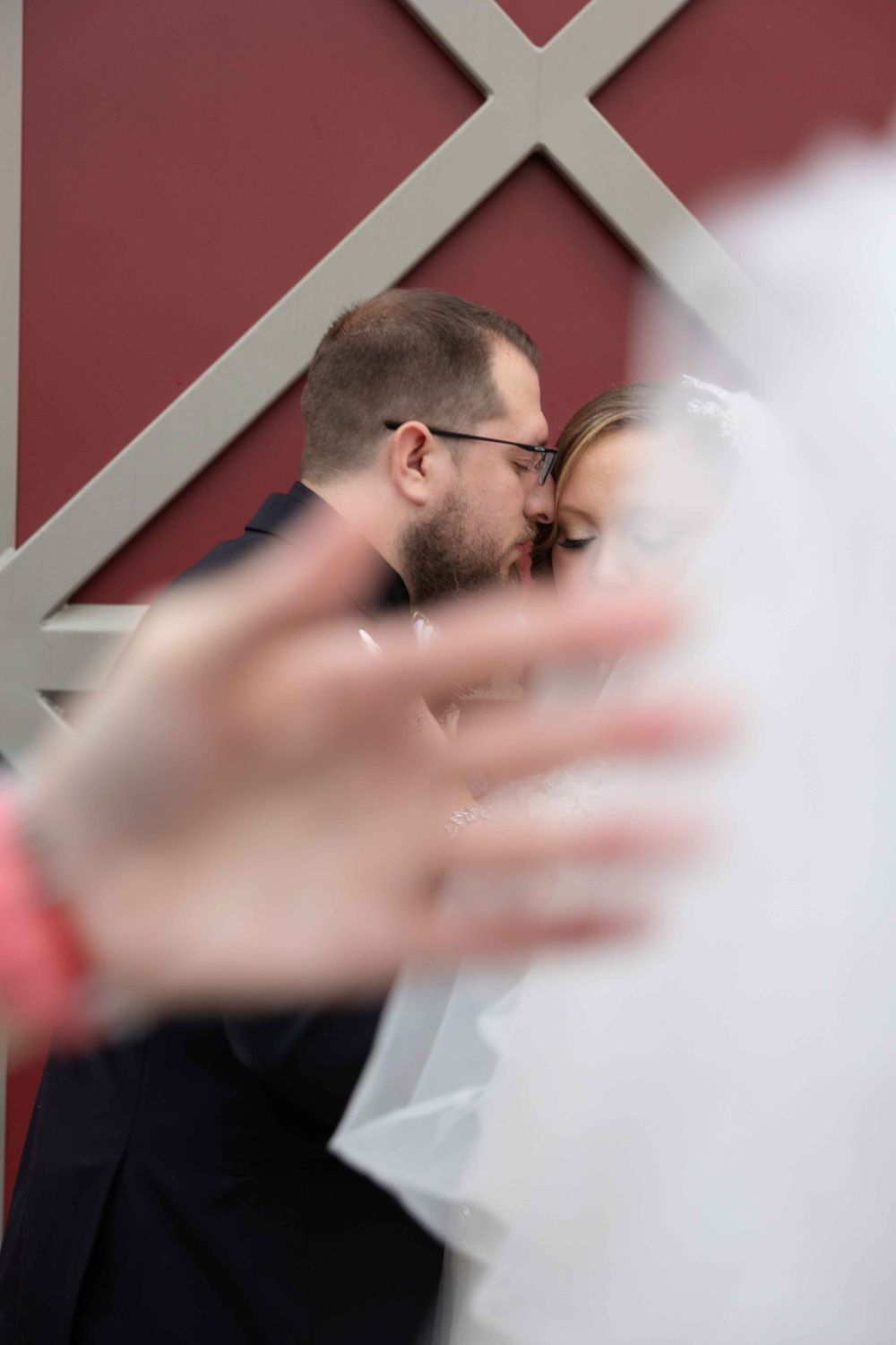 Intimate moment between newlyweds kissing against a red wall with white crossbeams.
