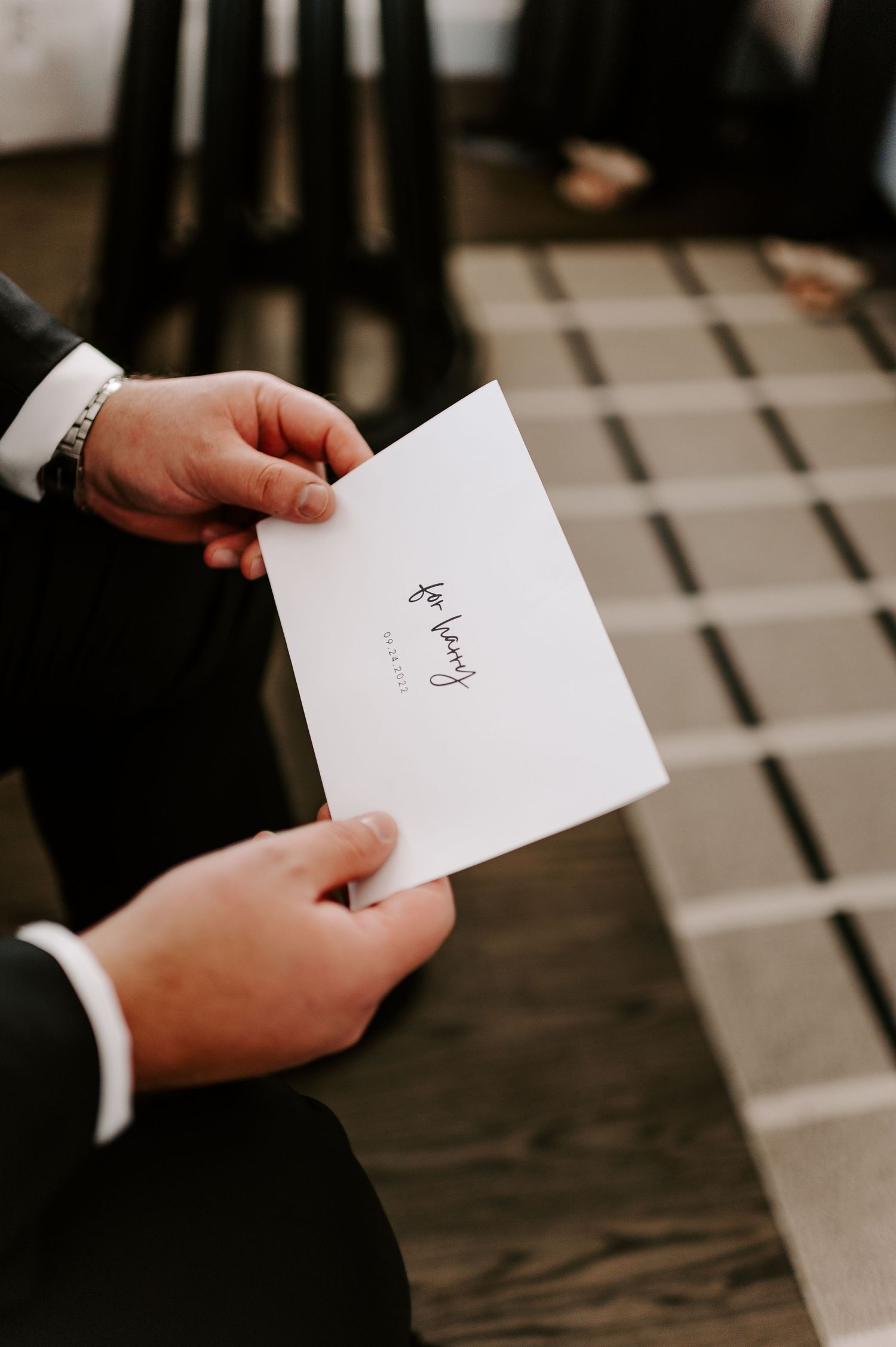 Hands holding a white envelope with handwritten text in an elegant setting.