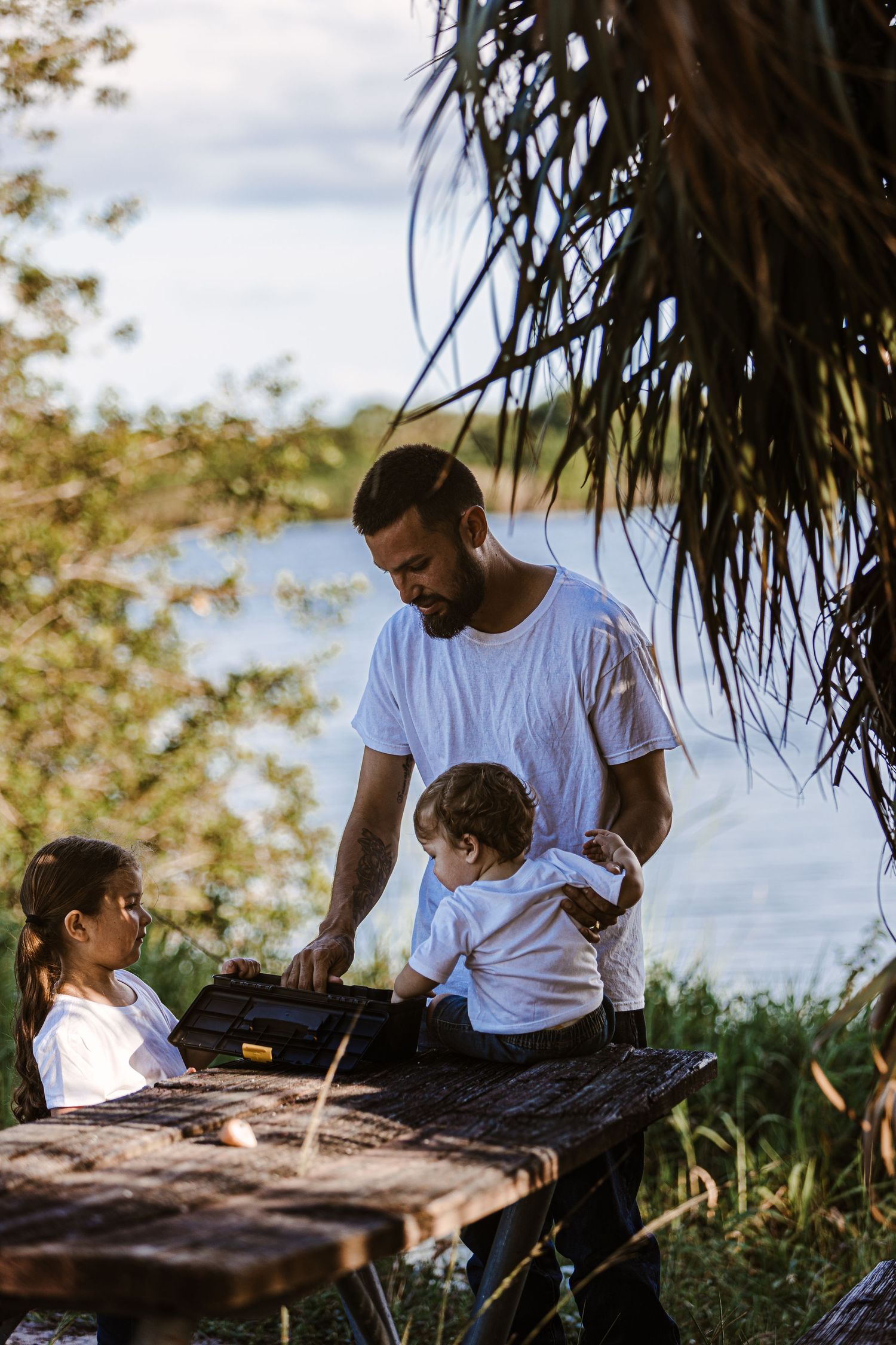 Family gathered around wooden table under palm trees outdoors.
