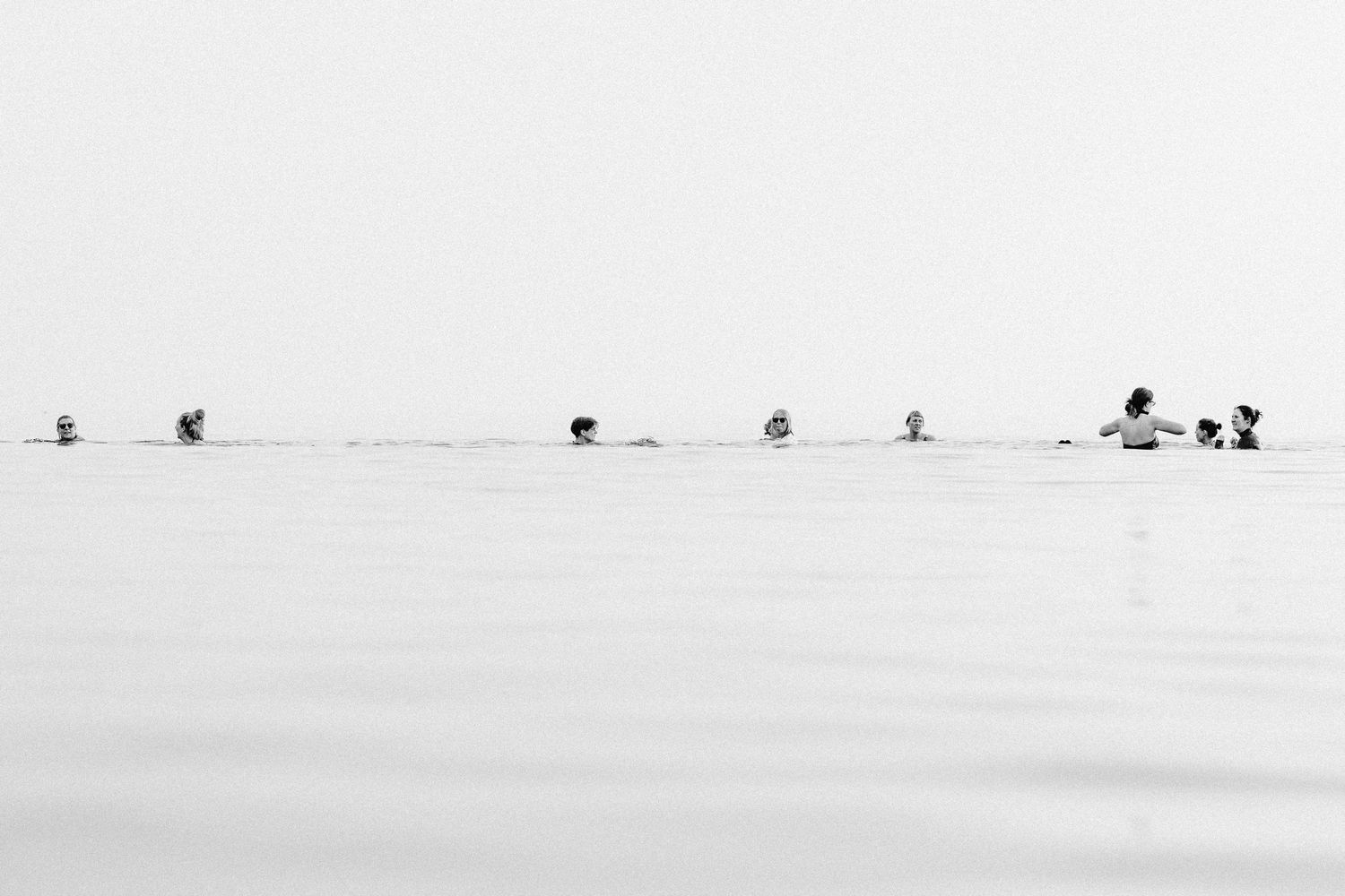Silhouettes of people walking along a minimalist white beach horizon.