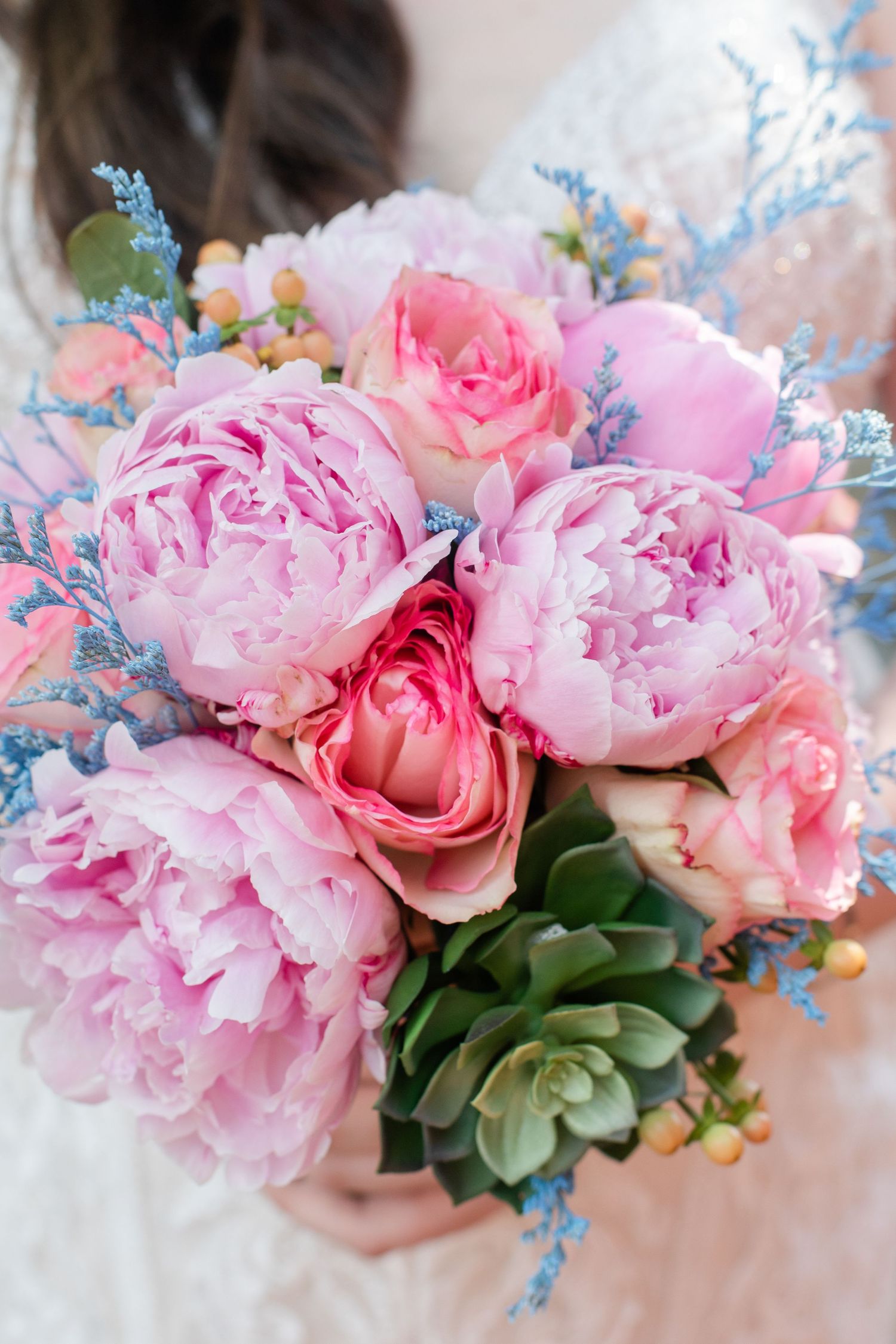 Elegant floral arrangement featuring pink peonies, roses, and blue delphinium with succulent accents.