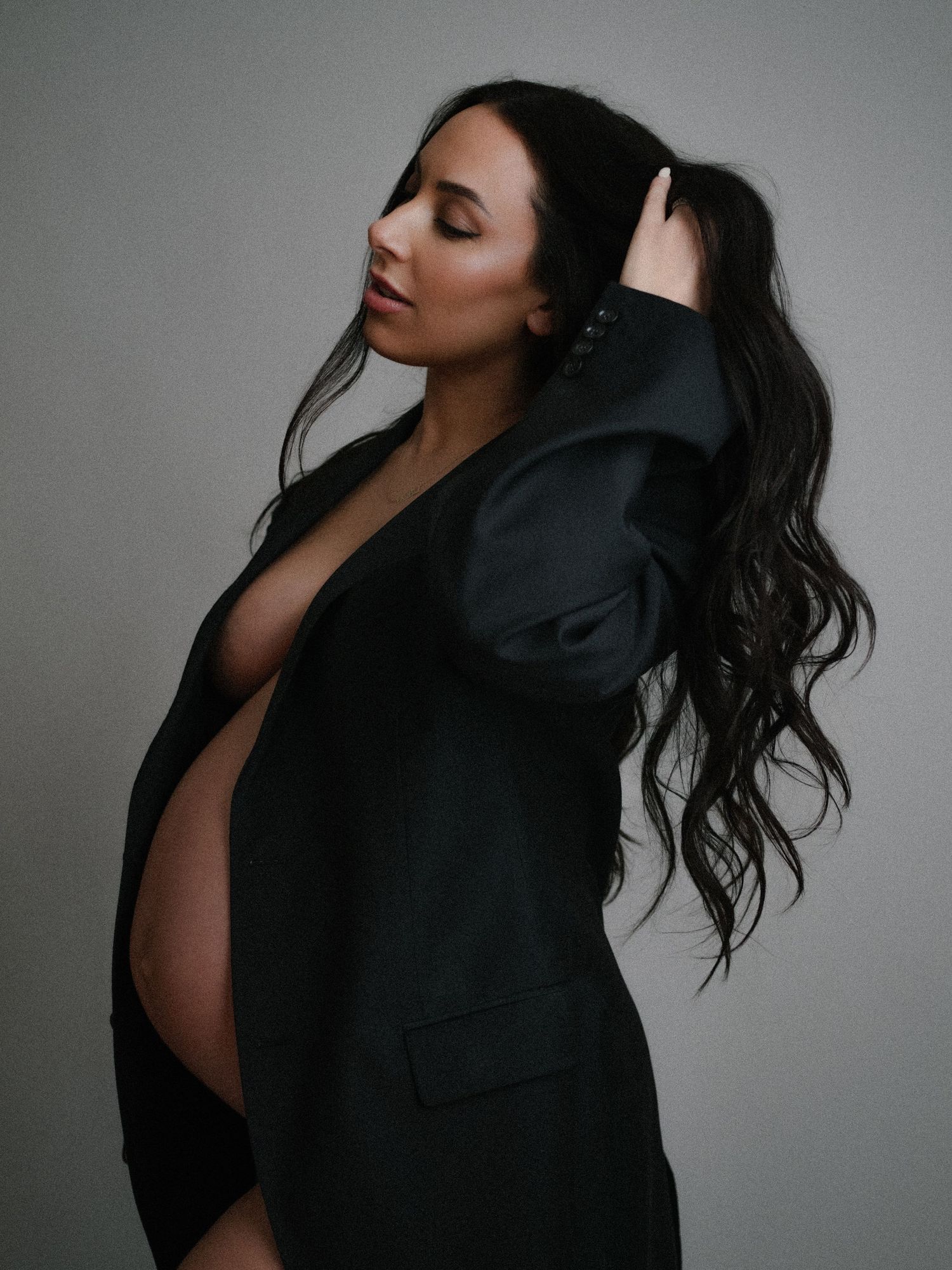 Artistic black and white maternity portrait series showing movement with a black blazer and flowing dark hair.