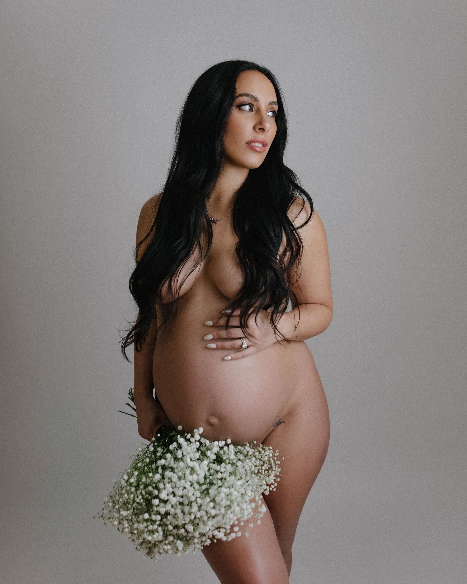 Elegant maternity portraits with baby's breath flowers against light studio background.