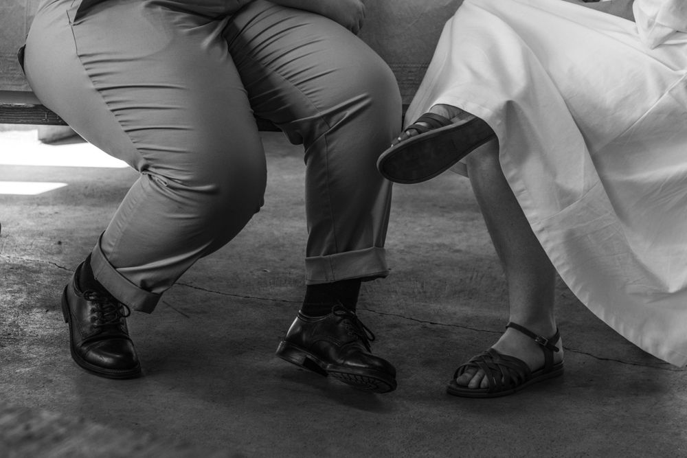 Small details of the newlywed couple, their legs and feet angled toward each other, photographed in black and white