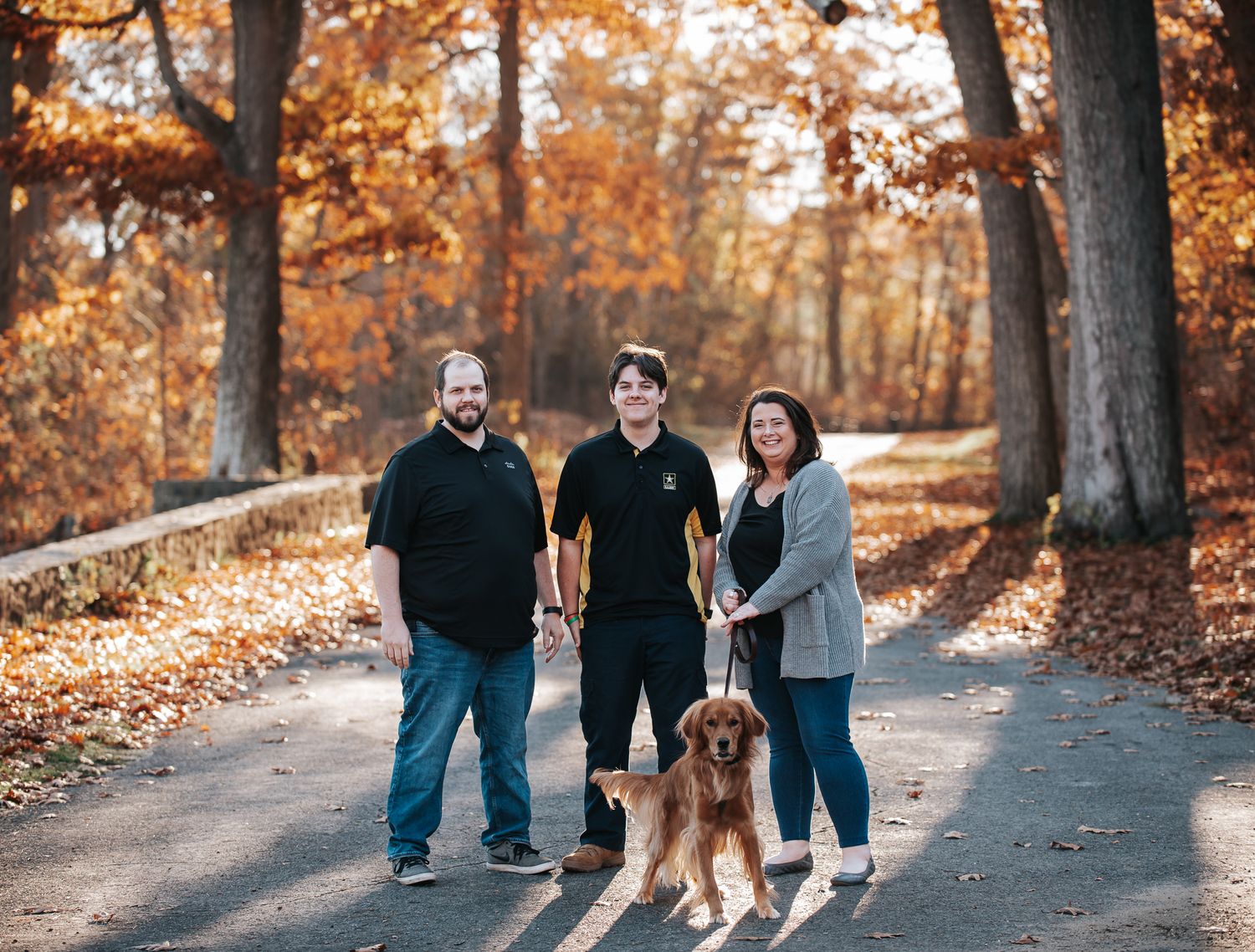 Family walking with their golden retriever on a path surrounded by autumn foliage.