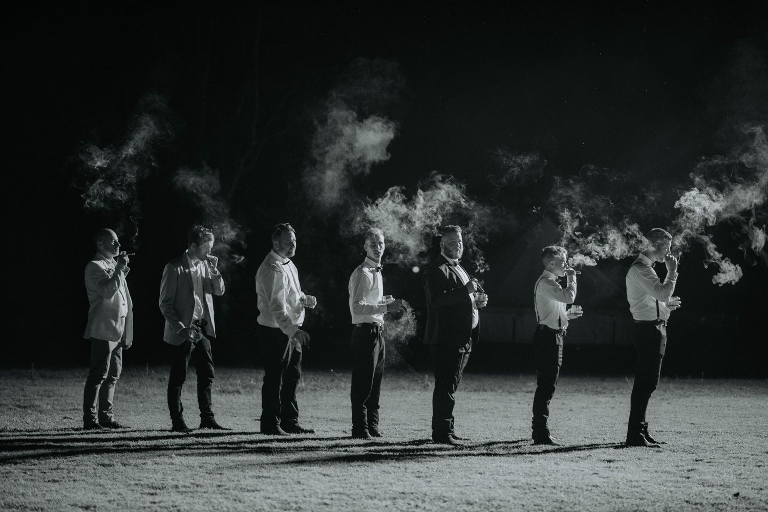 A black and white photo of groomsmen standing in a line creating dramatic smoke effects.