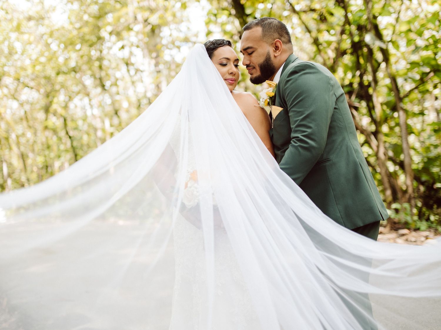 A romantic wedding moment captured with a flowing white veil in an outdoor setting.