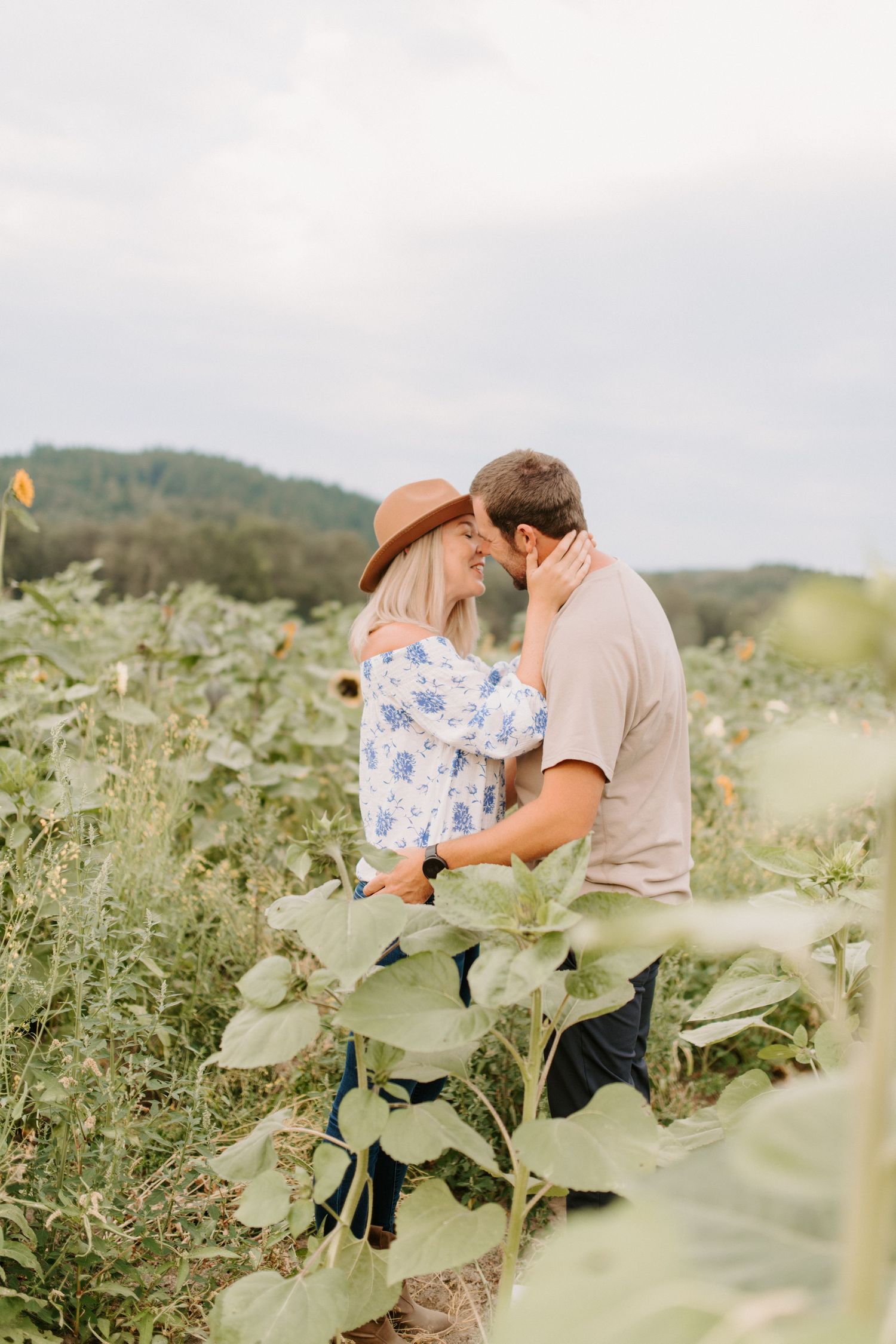 Couple embracing in field of wildflowers with mountains visible in background.