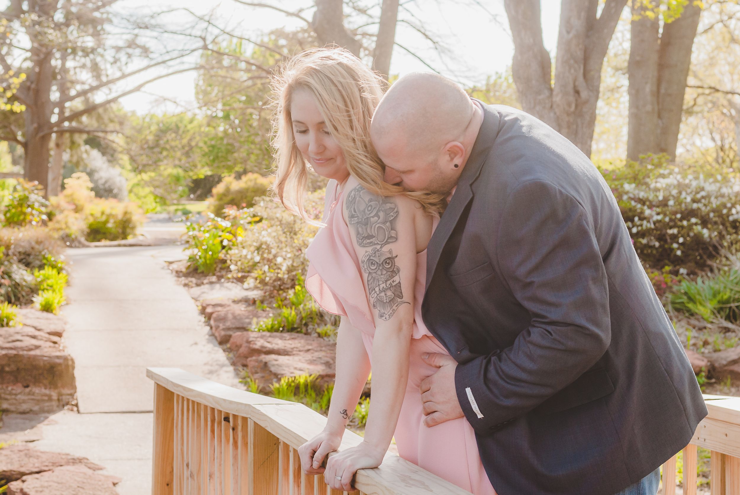 a portrait of a couple leaning over a bridge railing together with the man behind her and kissing her shoulder