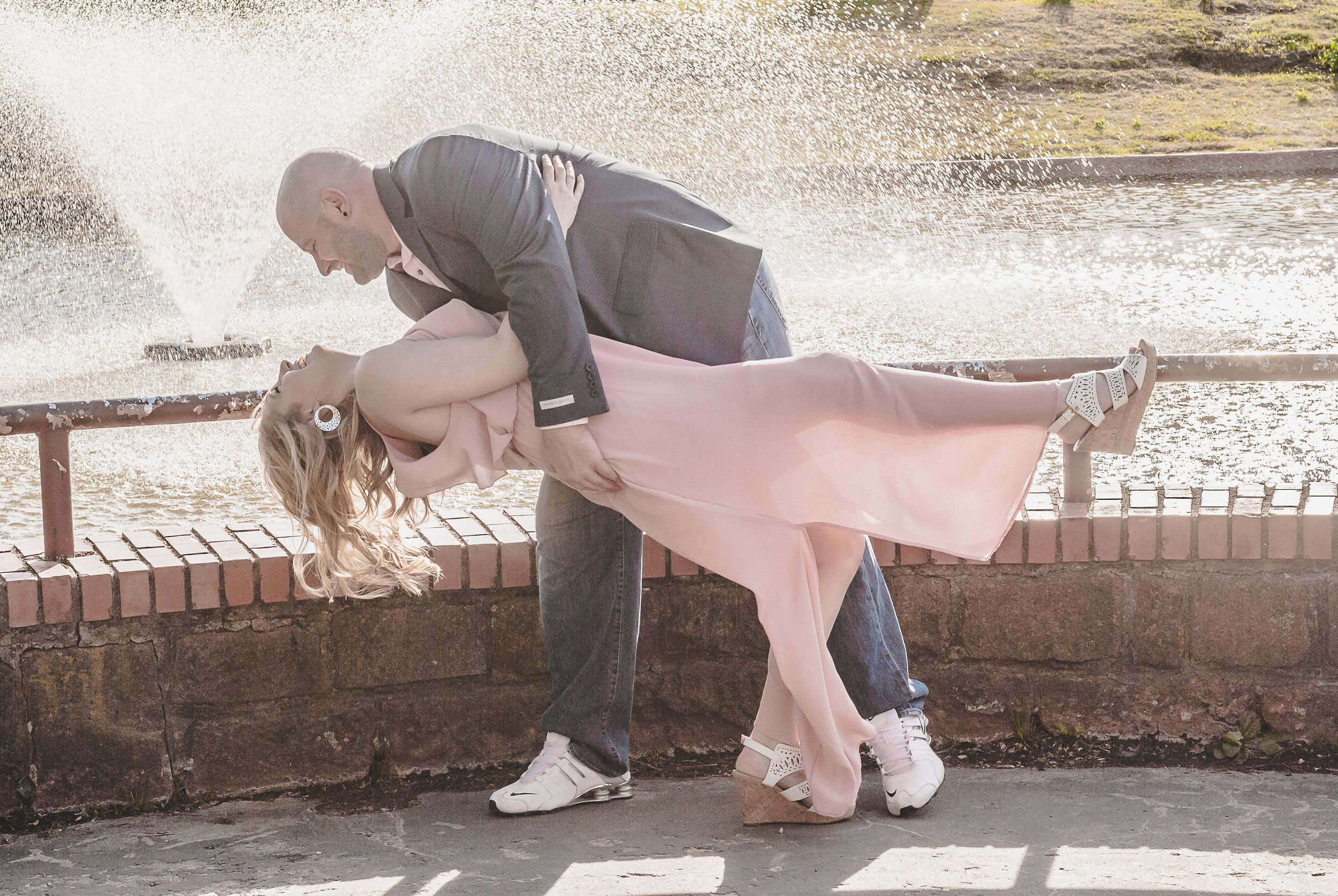 a portrait of a couple in front of a water fountain with the woman being dipped by the man