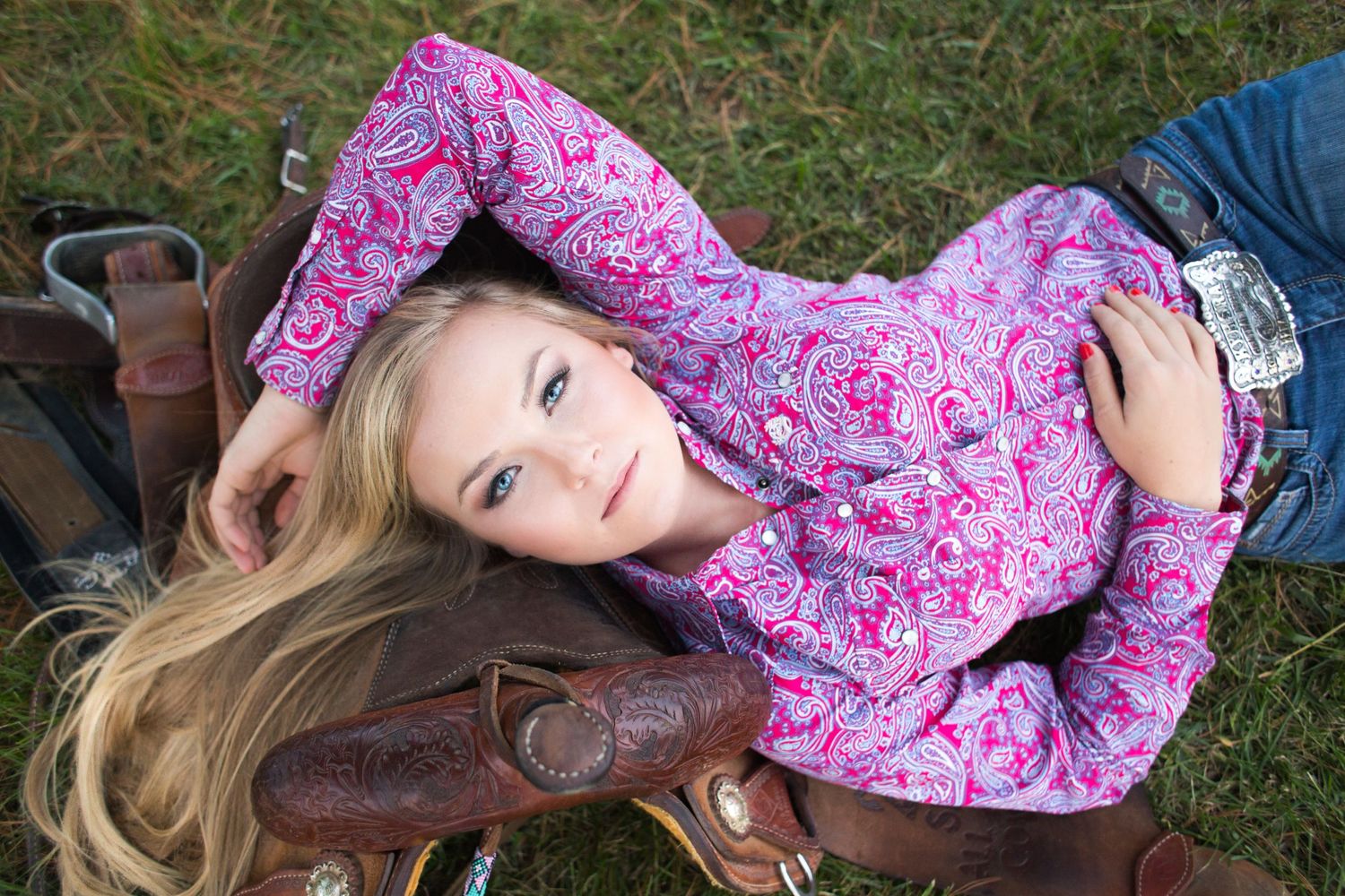 Portrait of person in pink patterned top lying on grass with leather boots.