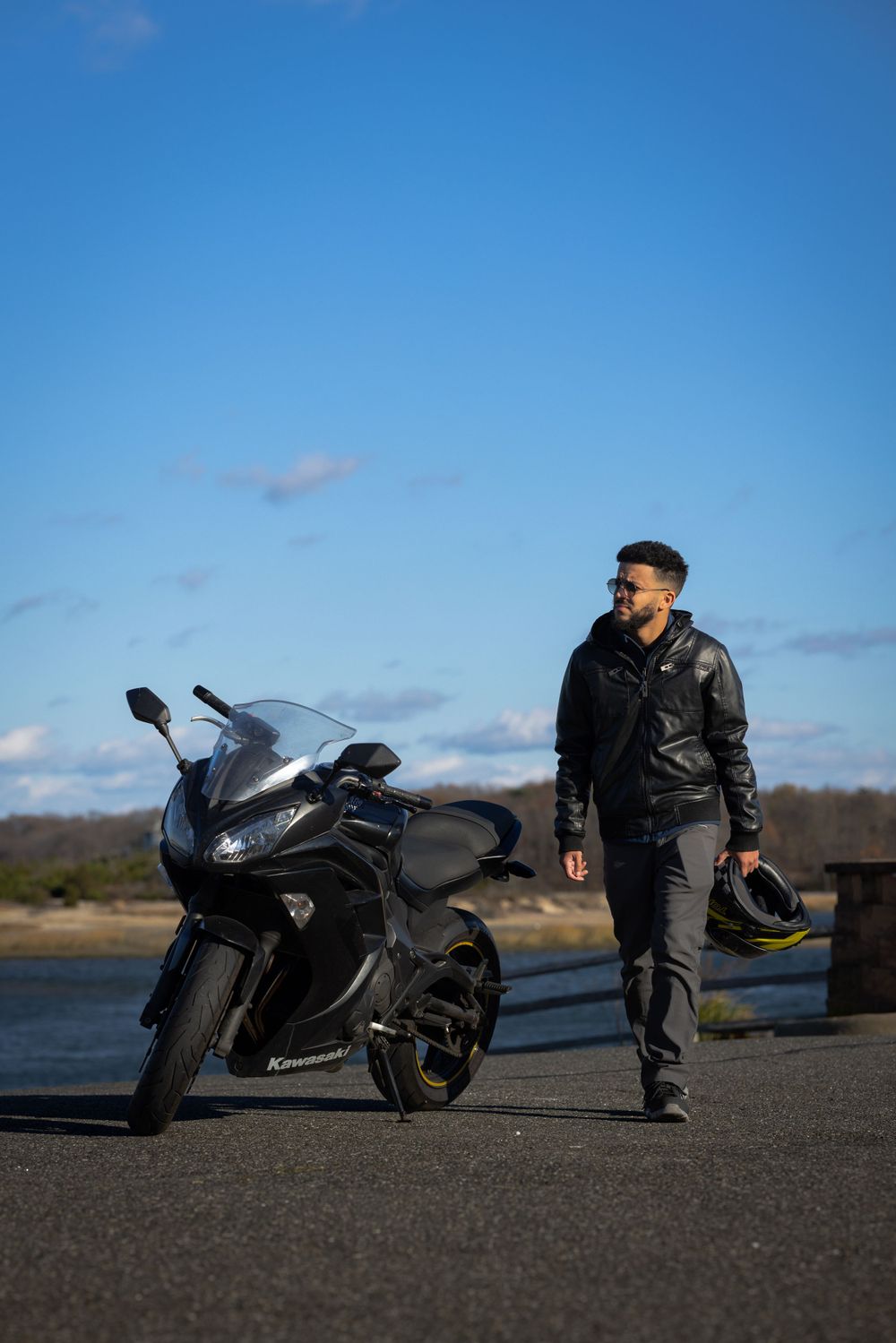 A black Kawasaki motorcycle parked on waterfront with rider in leather jacket.