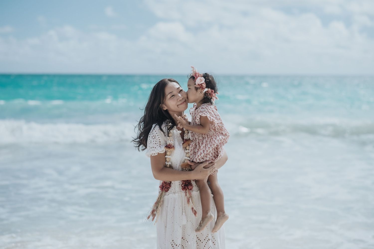 A mother lovingly holds her toddler daughter on a tropical beach with turquoise ocean waves in the background.
ハワイの人気フローリスト