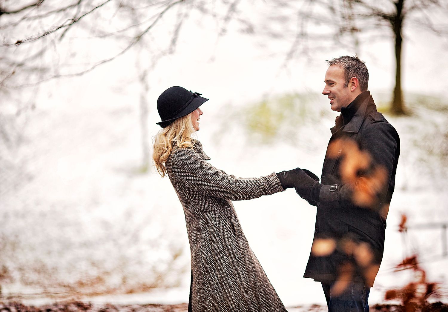 Engaged couple look at each other and hold hands in the park during Winter against a snowy landscape