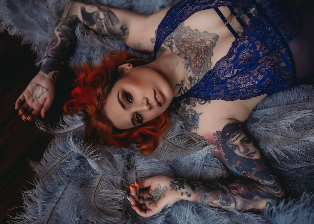 Artistic boudoir photo with red hair and blue lace against gray feathers.