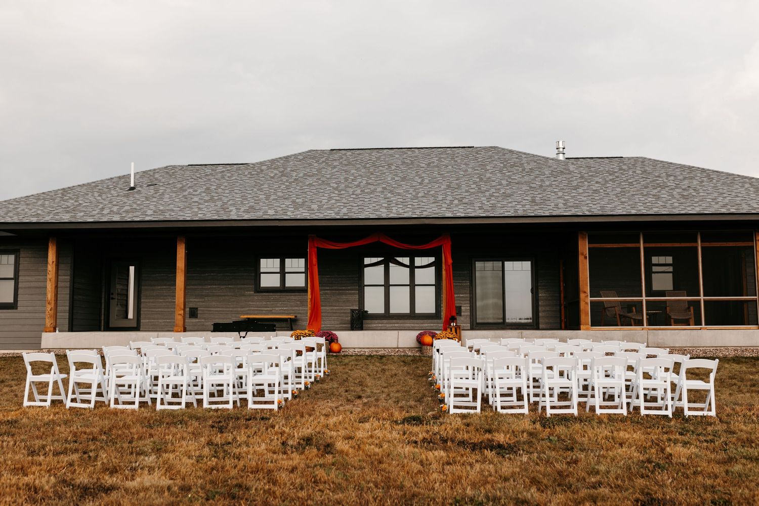 White chairs set up for an outdoor wedding ceremony in front of a modern gray house with wooden posts.