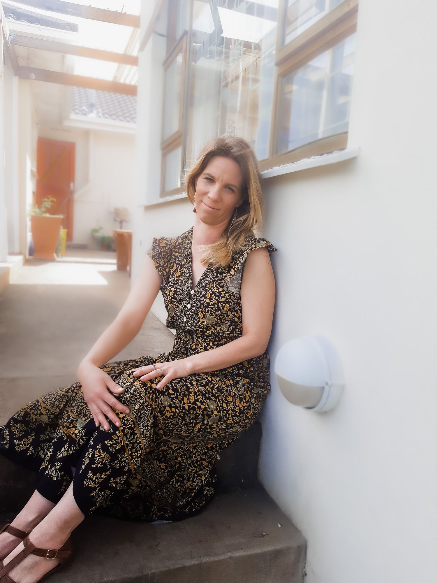 Person in floral dress sitting on steps in sunlit indoor space.