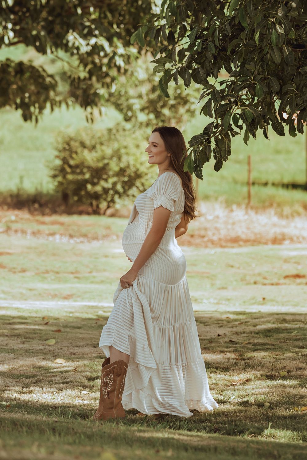 A serene outdoor maternity portrait in a flowing white dress under a tree.