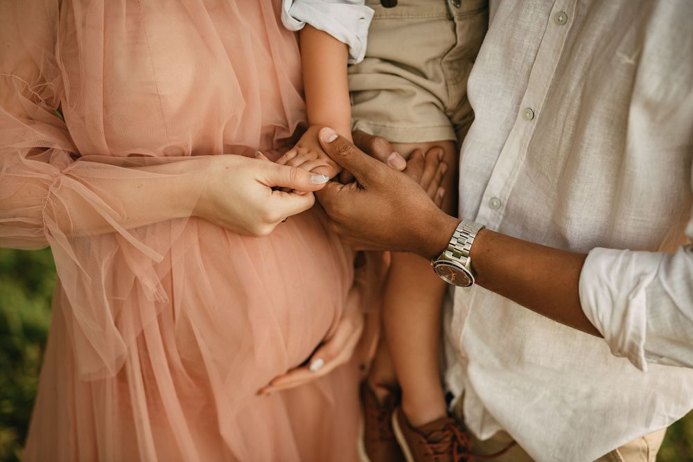 Close-up of hands exchanging rings during an intimate outdoor ceremony with soft pink and white attire.