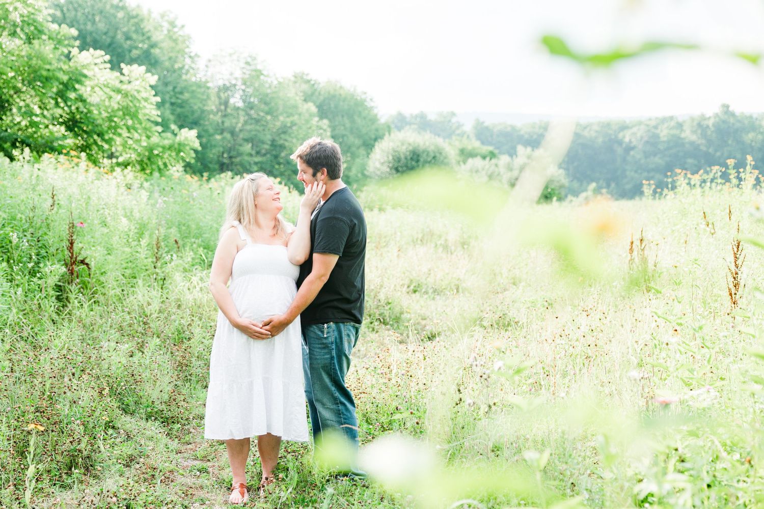 A romantic couple embraces in a sunlit meadow with soft focus wildflowers in the foreground.