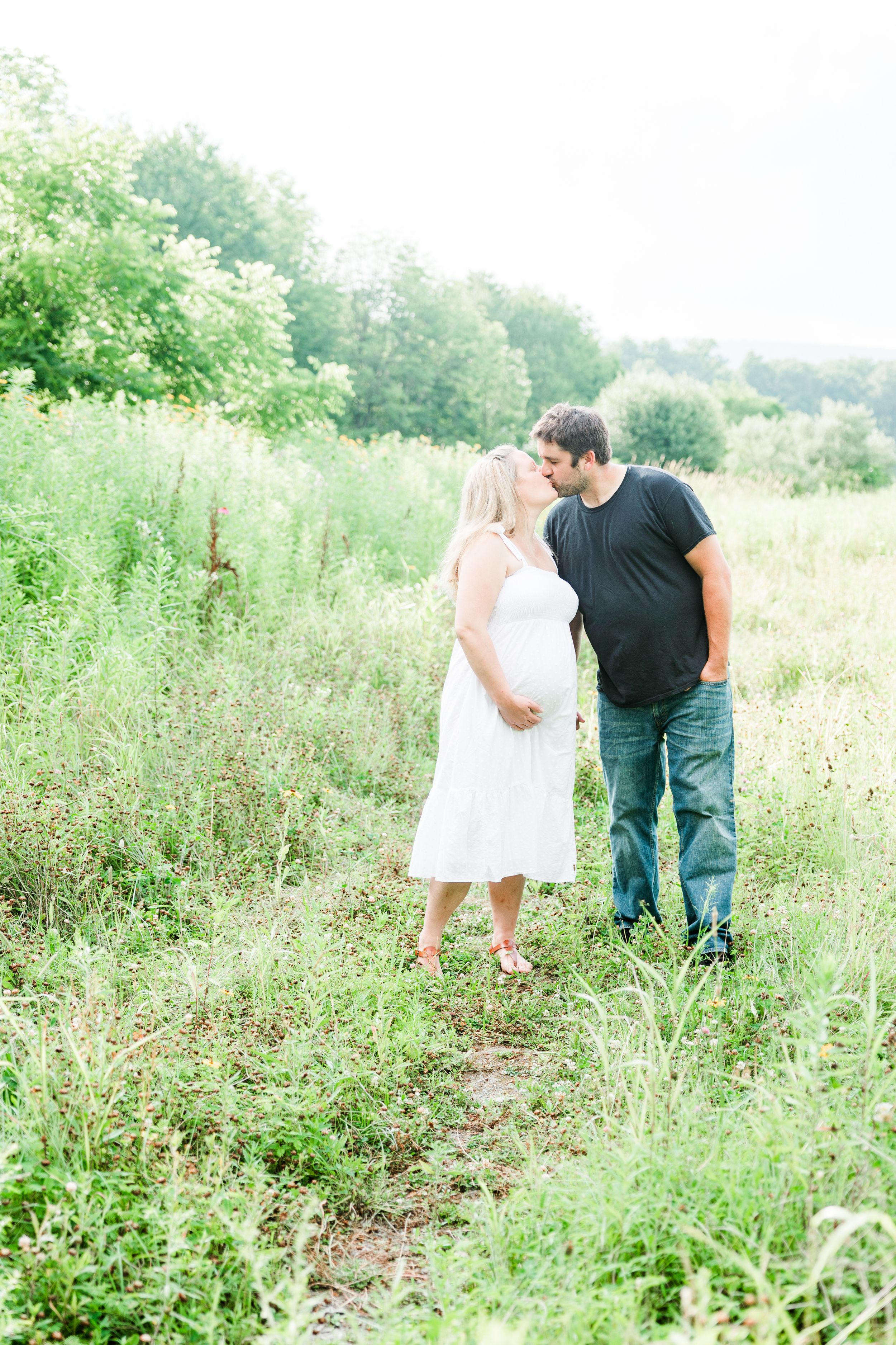 A couple shares a tender moment while standing in a lush green summer field.