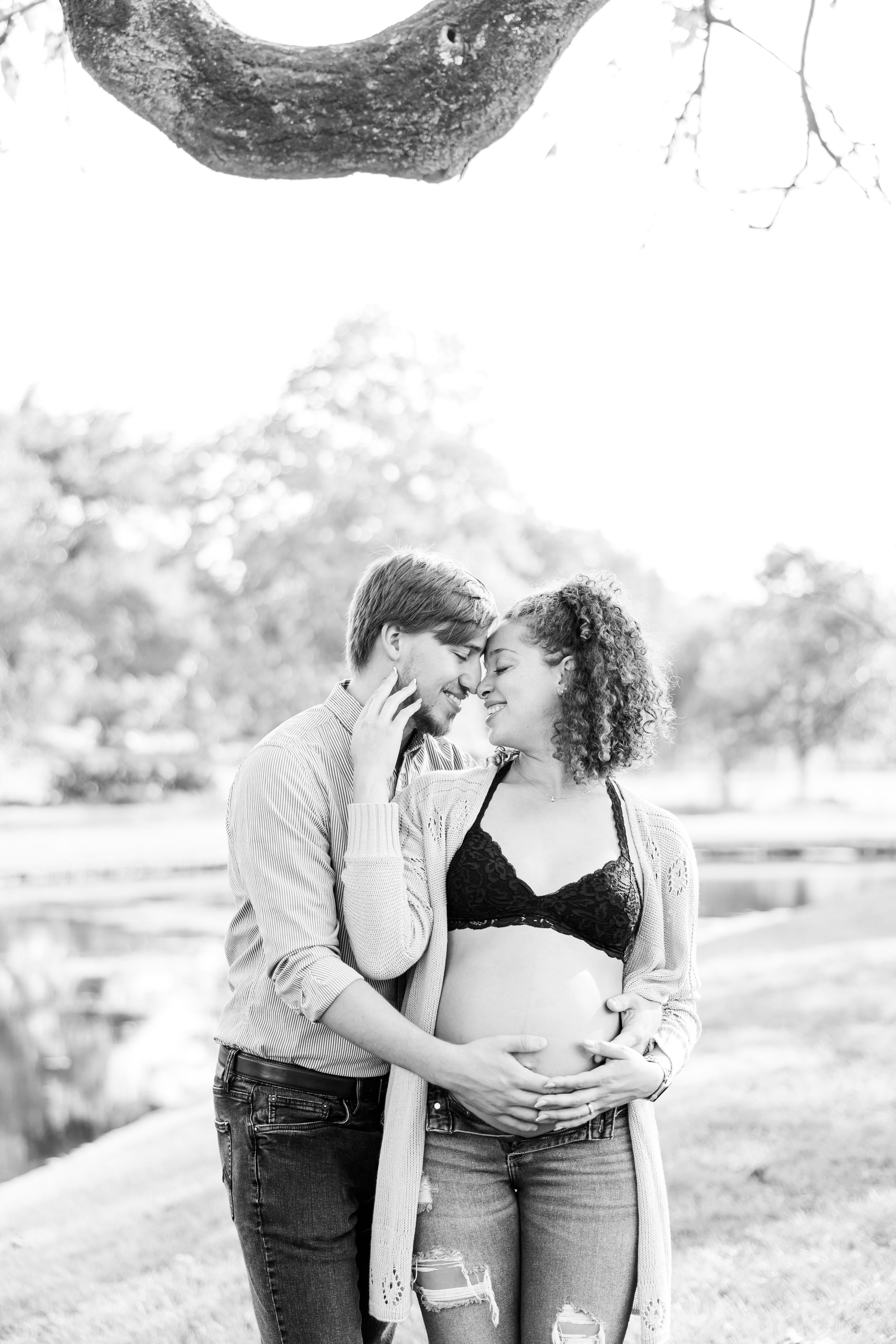 A tender black and white maternity photo of a couple sharing an intimate moment outdoors.