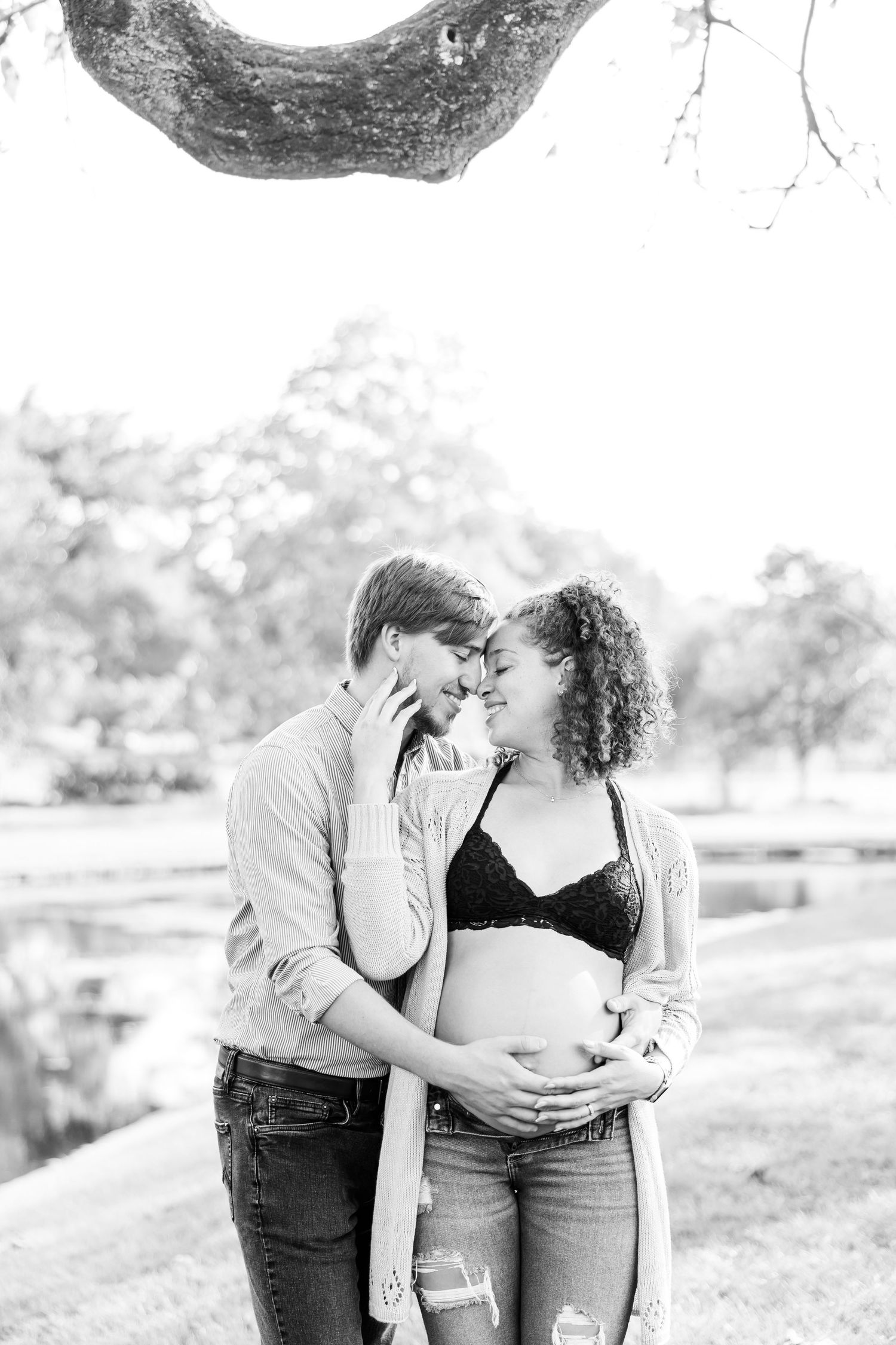 A tender black and white maternity photo of a couple sharing an intimate moment outdoors.