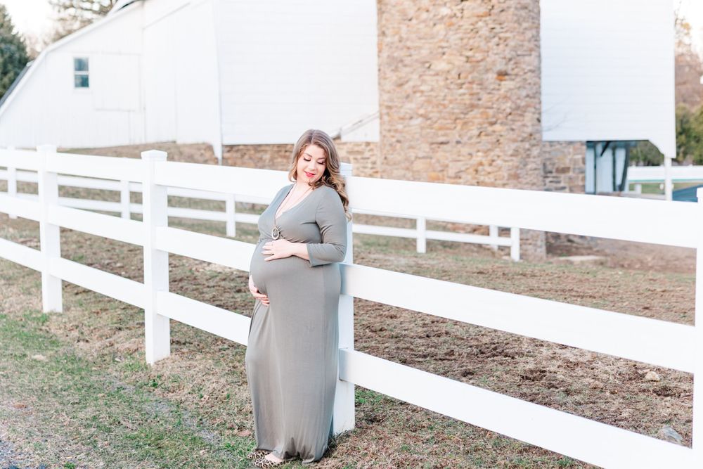 Maternity portrait against a white fence and stone wall background.