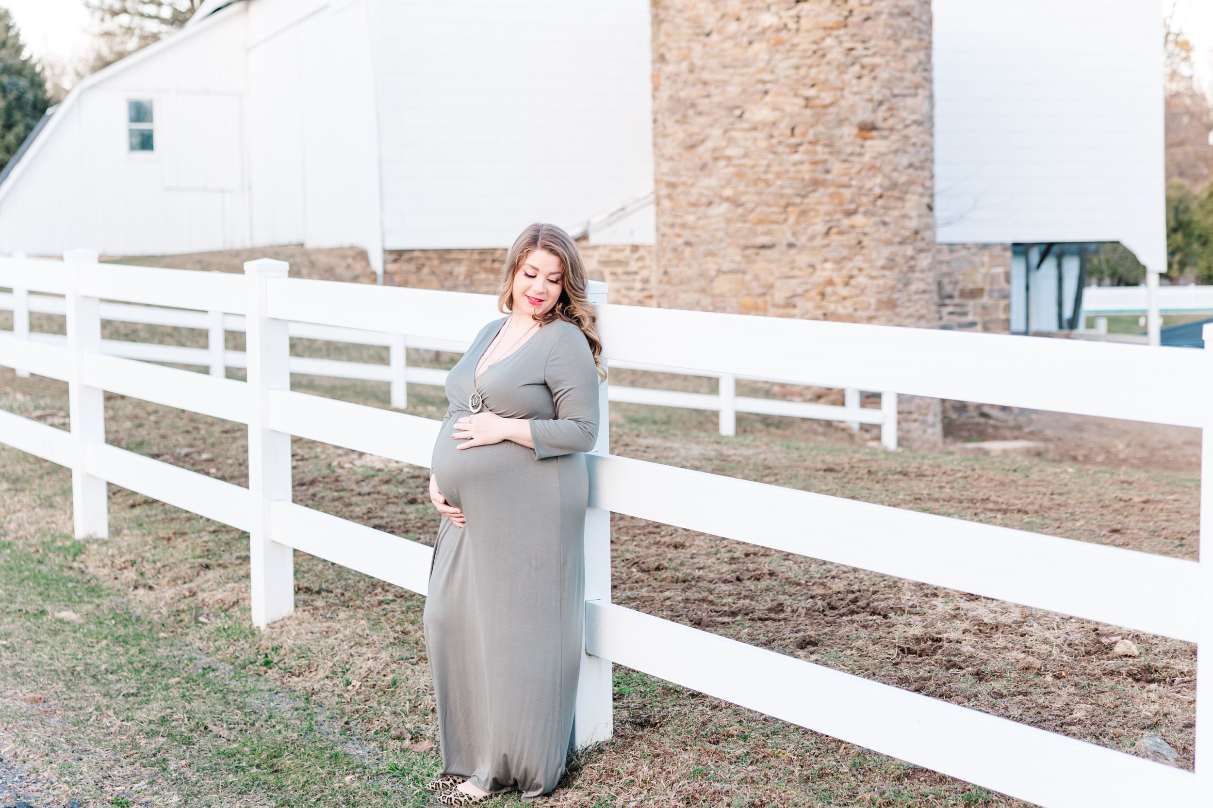 Maternity portrait against a white fence and stone wall background.