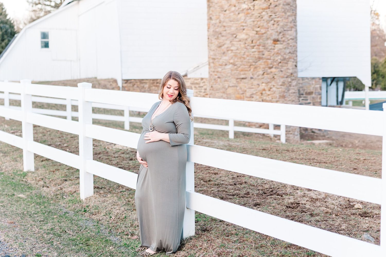 Maternity portrait against a white fence and stone wall background.