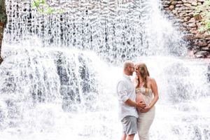 Intimate maternity portrait against dramatic cascading waterfall in natural setting.