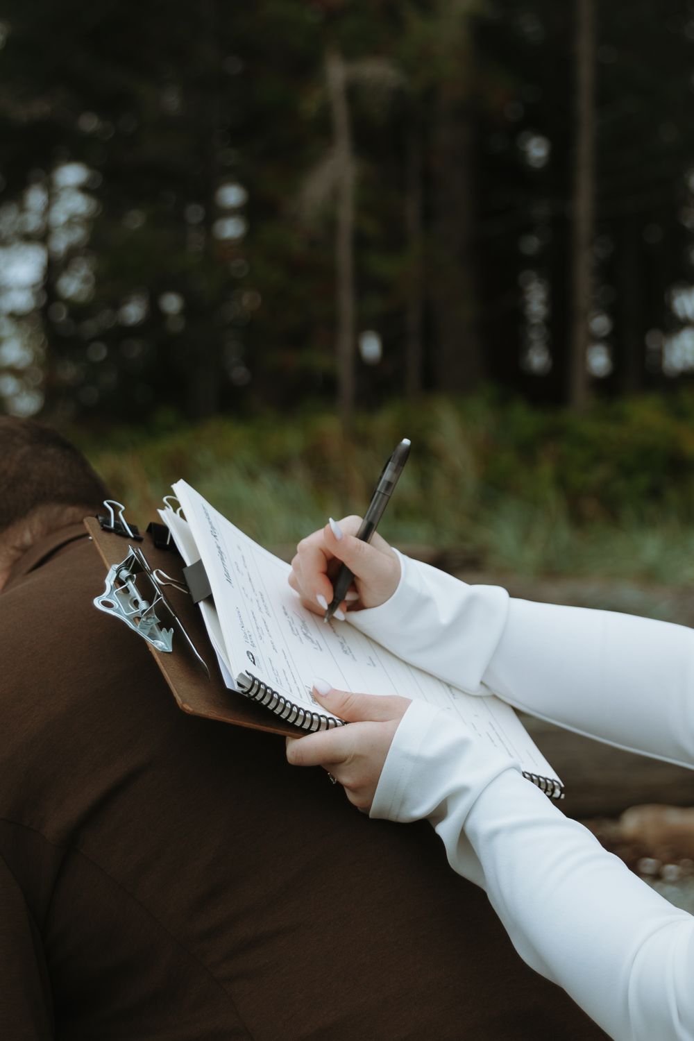 Hands in white and brown sleeves writing on a clipboard outdoors.