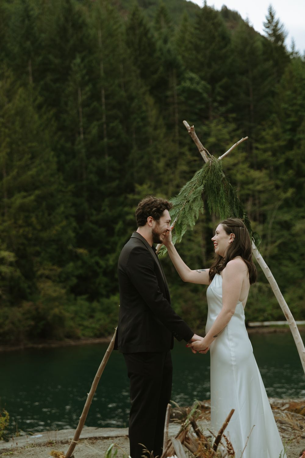 A wedding ceremony under a rustic wooden arch beside a serene mountain lake.