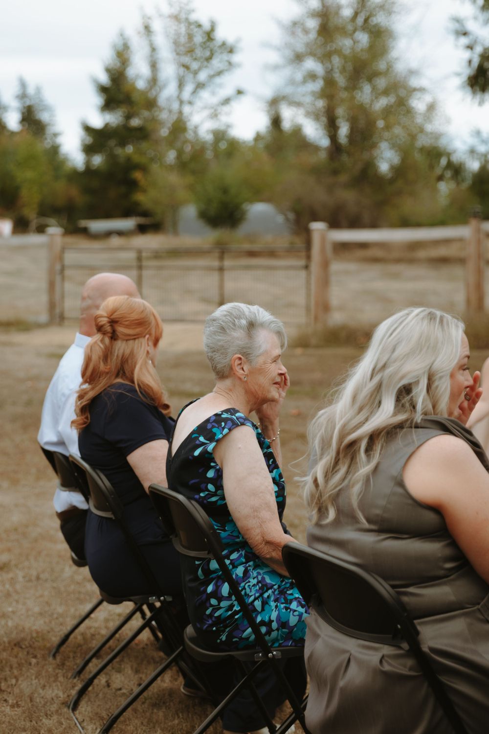 Wedding guests laughing together while seated in folding chairs outdoors.