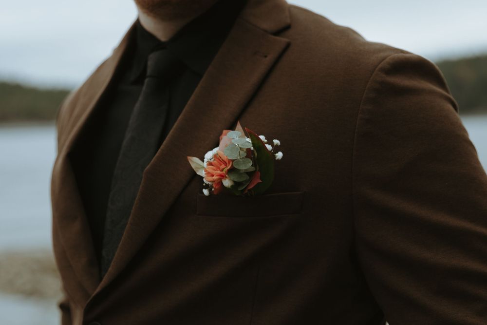 Close-up of a brown suit jacket with a delicate coral and white floral boutonniere.