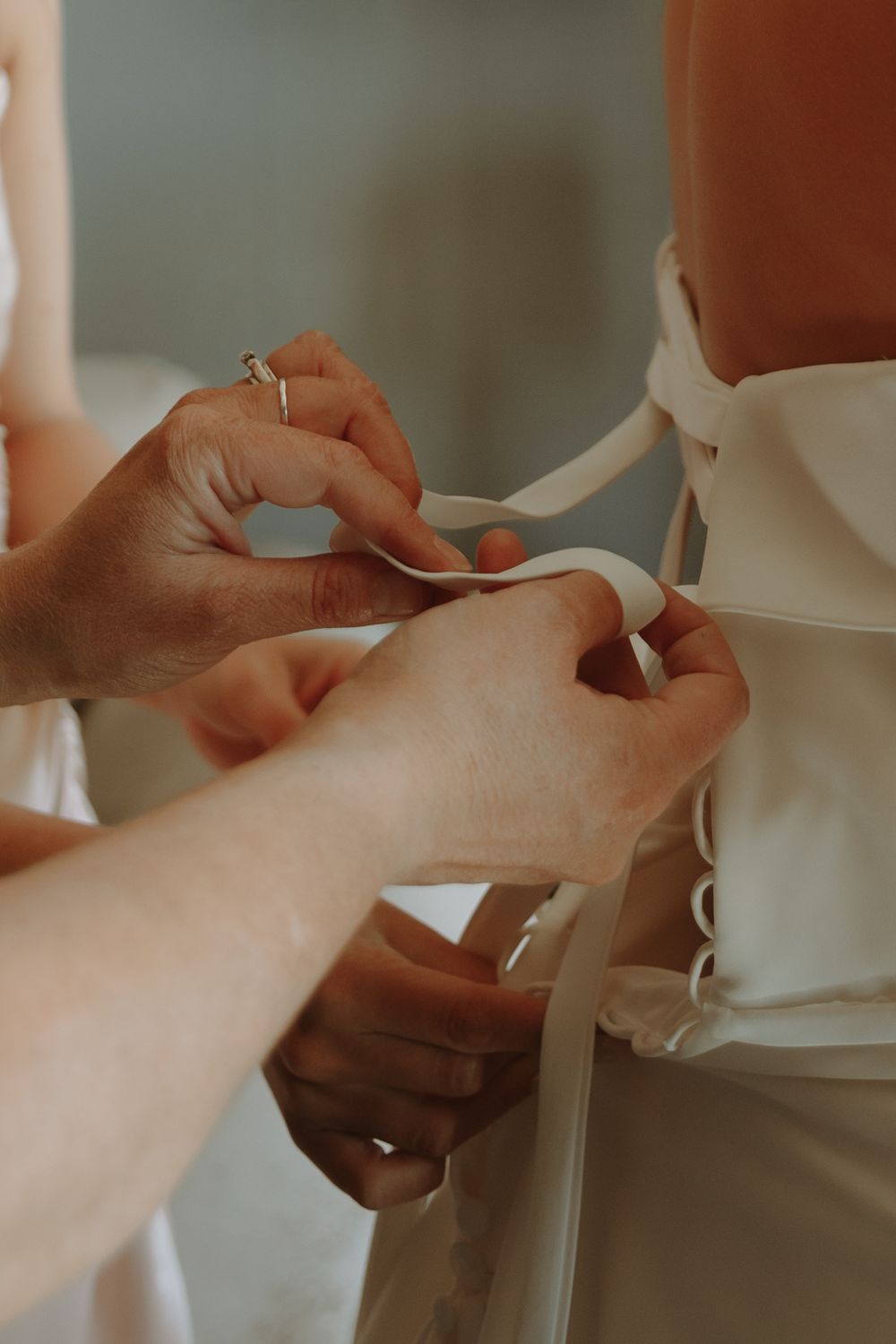 Close-up of hands lacing up a white wedding dress.