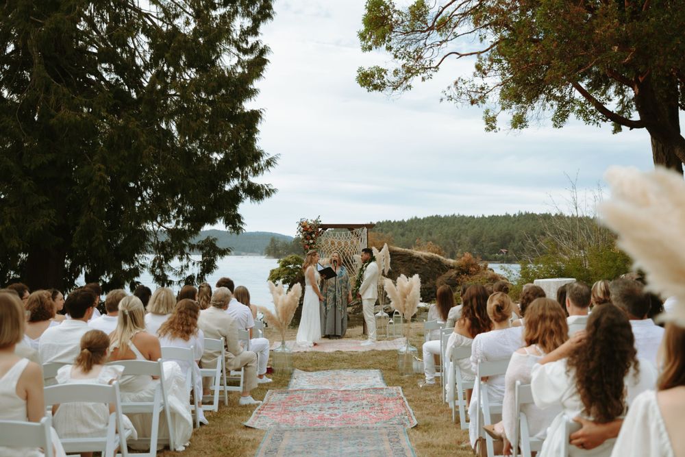 An outdoor wedding ceremony setup with white chairs and a floral arch overlooking the water.