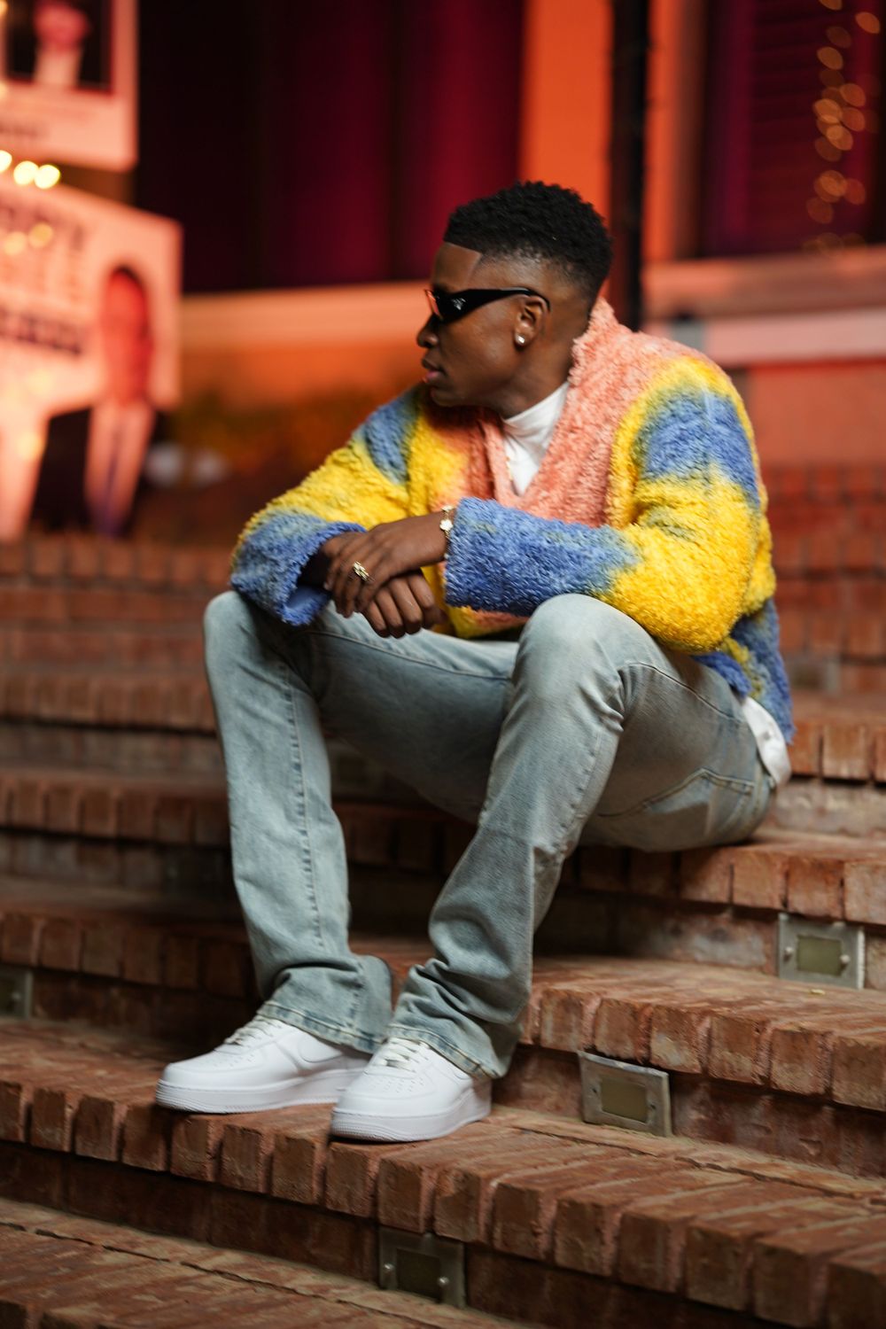 A contemplative pose on brick steps featuring a colorful fleece sweater and casual streetwear.