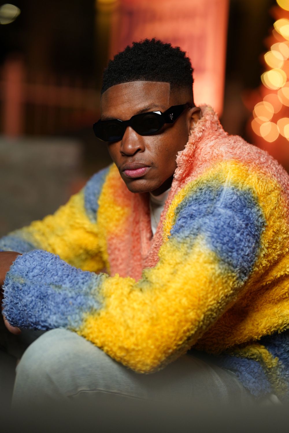 A close-up portrait showcasing a multicolored fuzzy sweater and sunglasses at night.