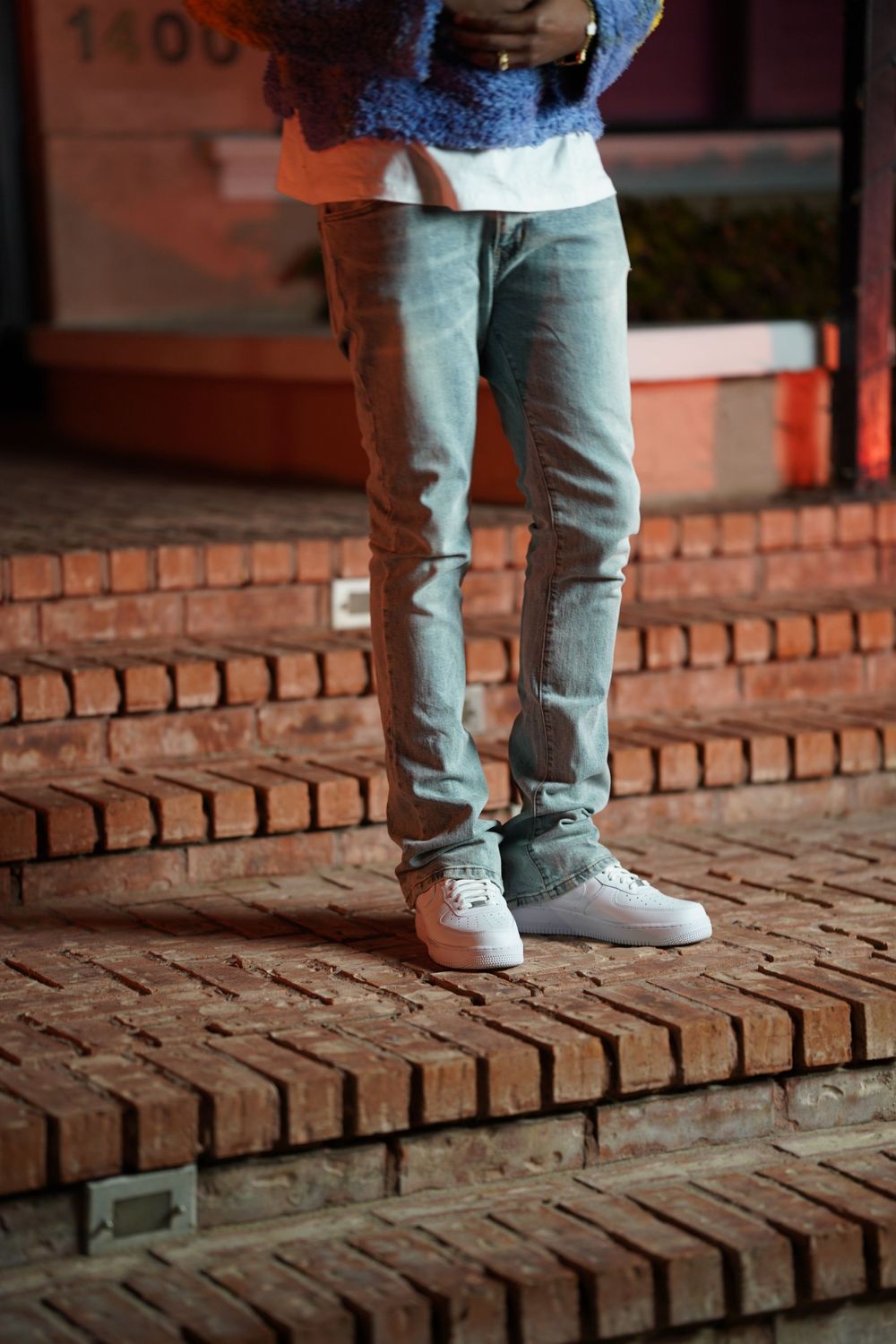 Light denim jeans and white sneakers standing on brick steps in evening lighting.